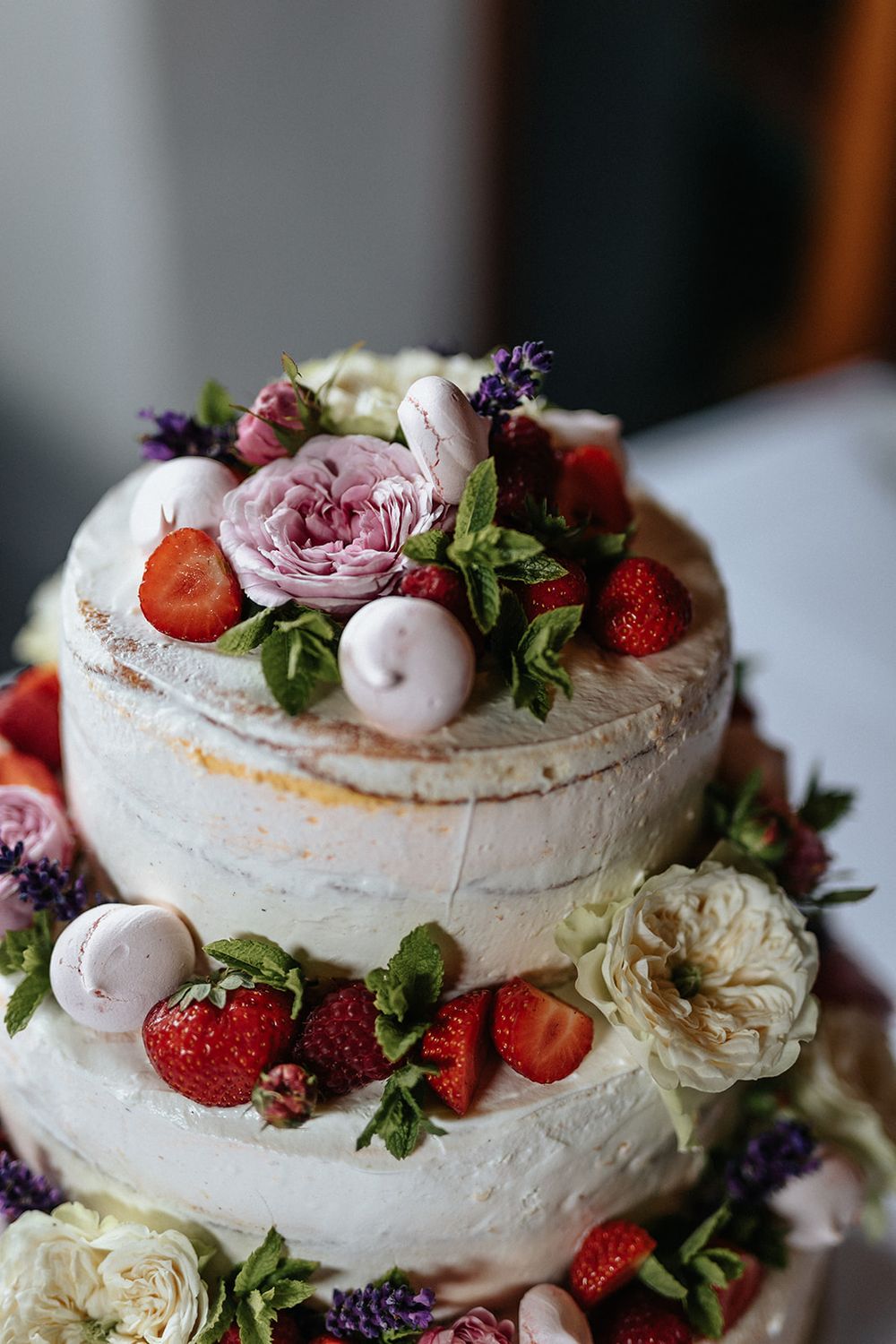 A layered pavlova cake decorated with fresh strawberries, white meringue kisses, and delicate pink roses.