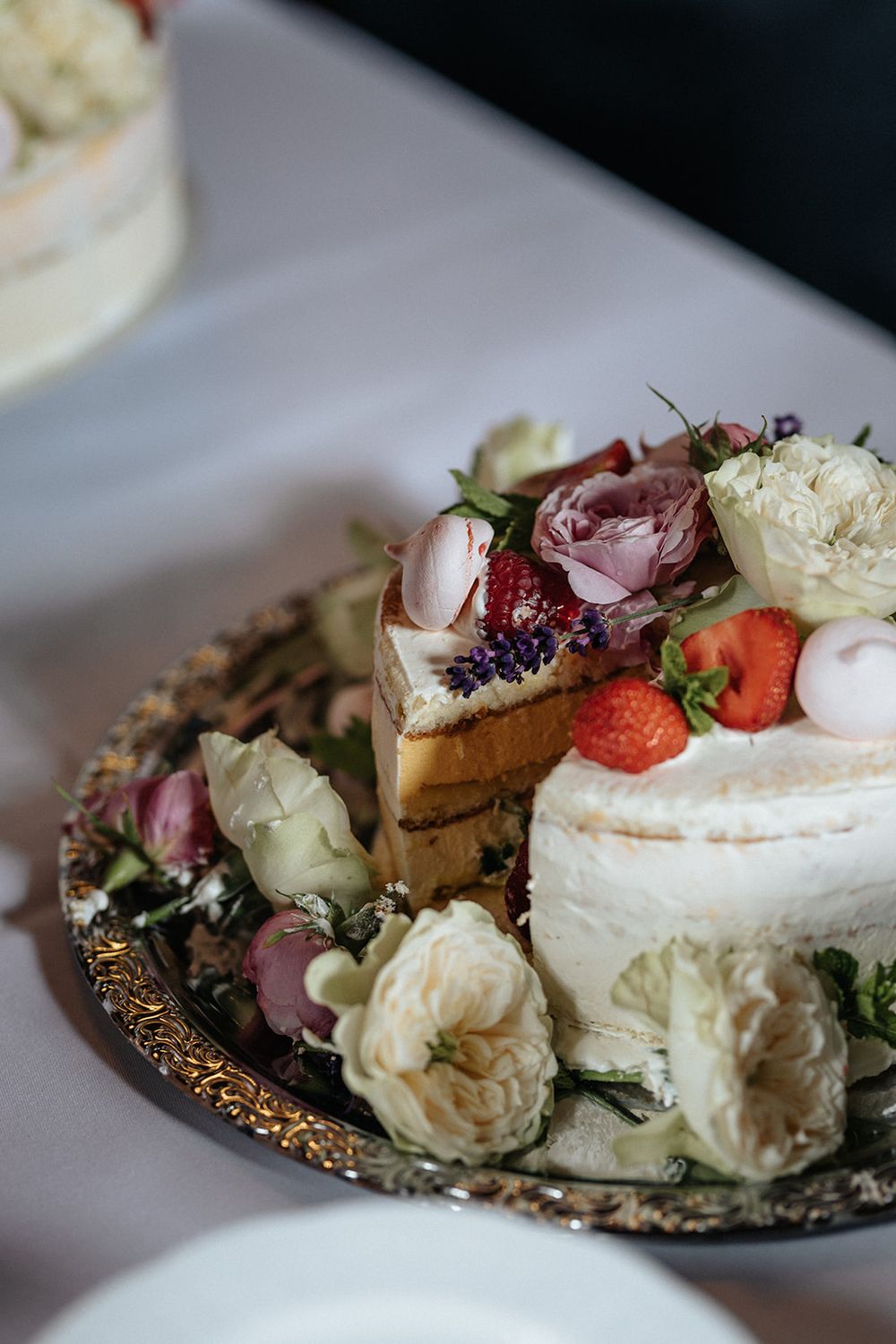 Elegant dessert plate featuring sliced cake decorated with fresh strawberries, pink roses, and white floral accents.