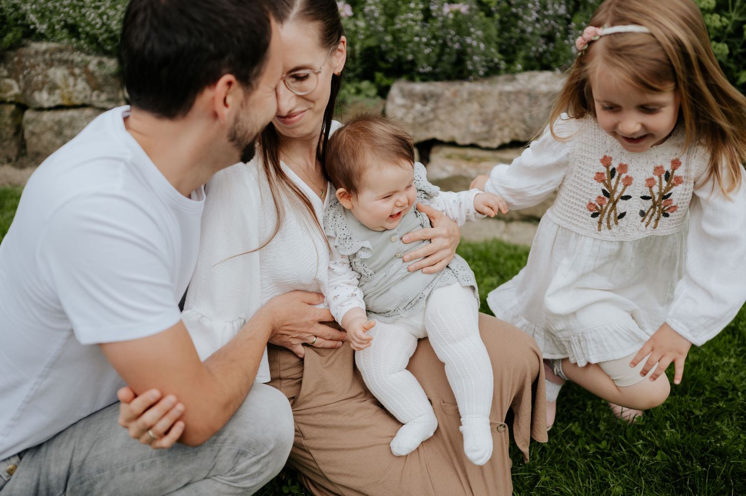 Eine Familie in weißen und neutralen Farbtönen sitzt gemeinsam im Freien in einem Garten für intime Porträts.