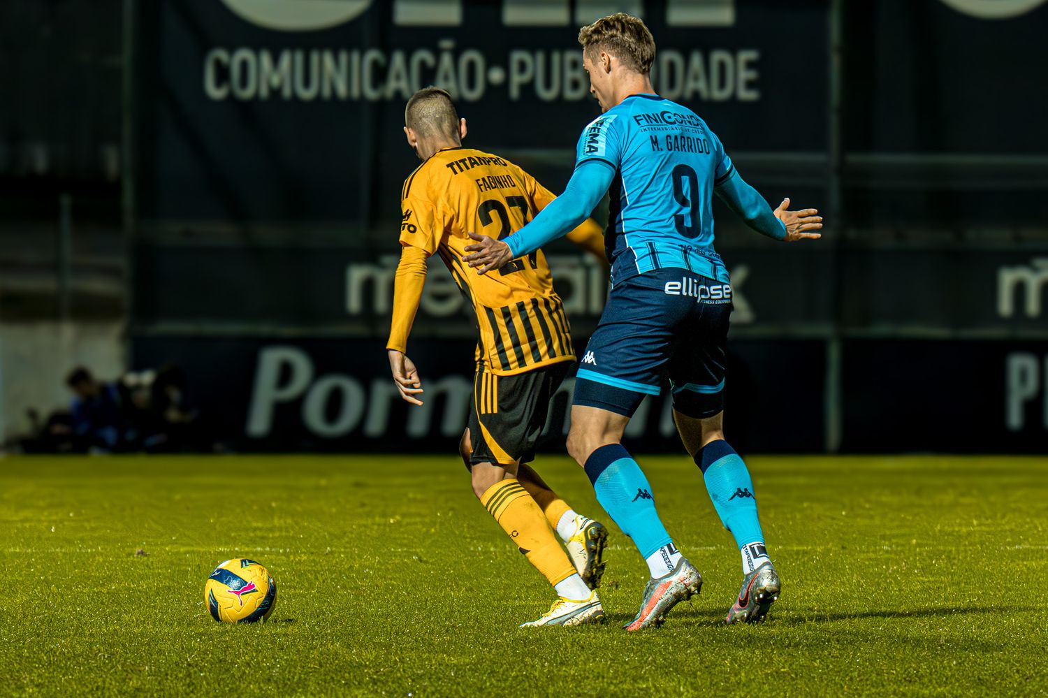 Soccer match action shot under stadium lights with players competing for the ball.
