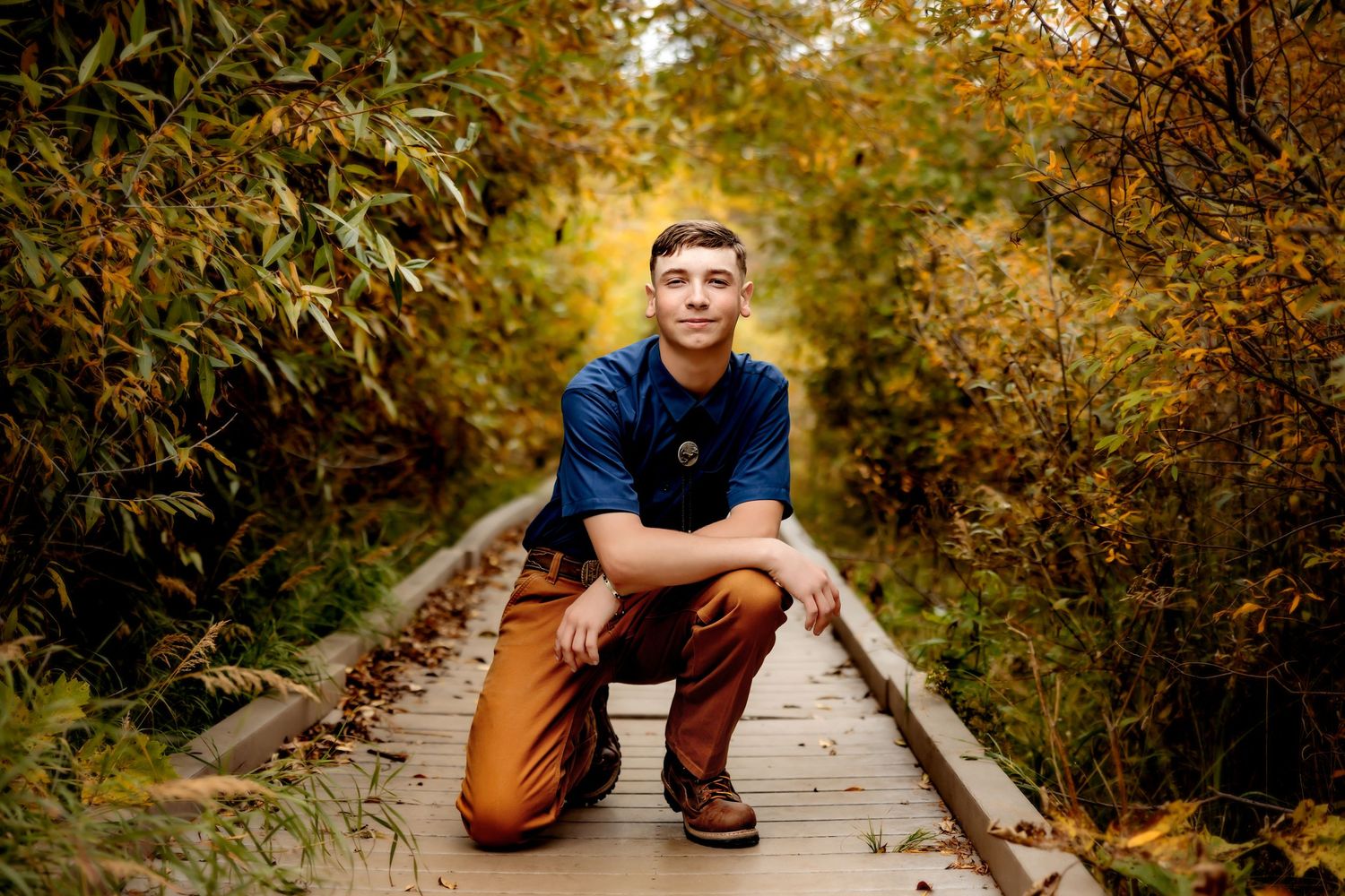 A person sits on a wooden boardwalk surrounded by vibrant autumn foliage in golden evening light.