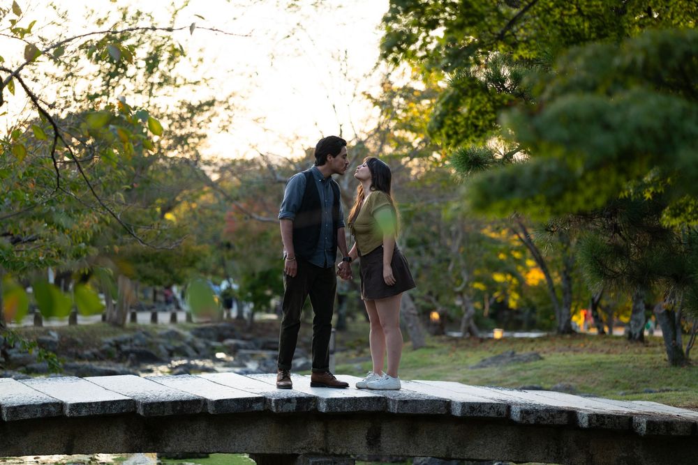 Couple sharing a romantic kiss on a stone bridge in a lush Japanese garden at golden hour.