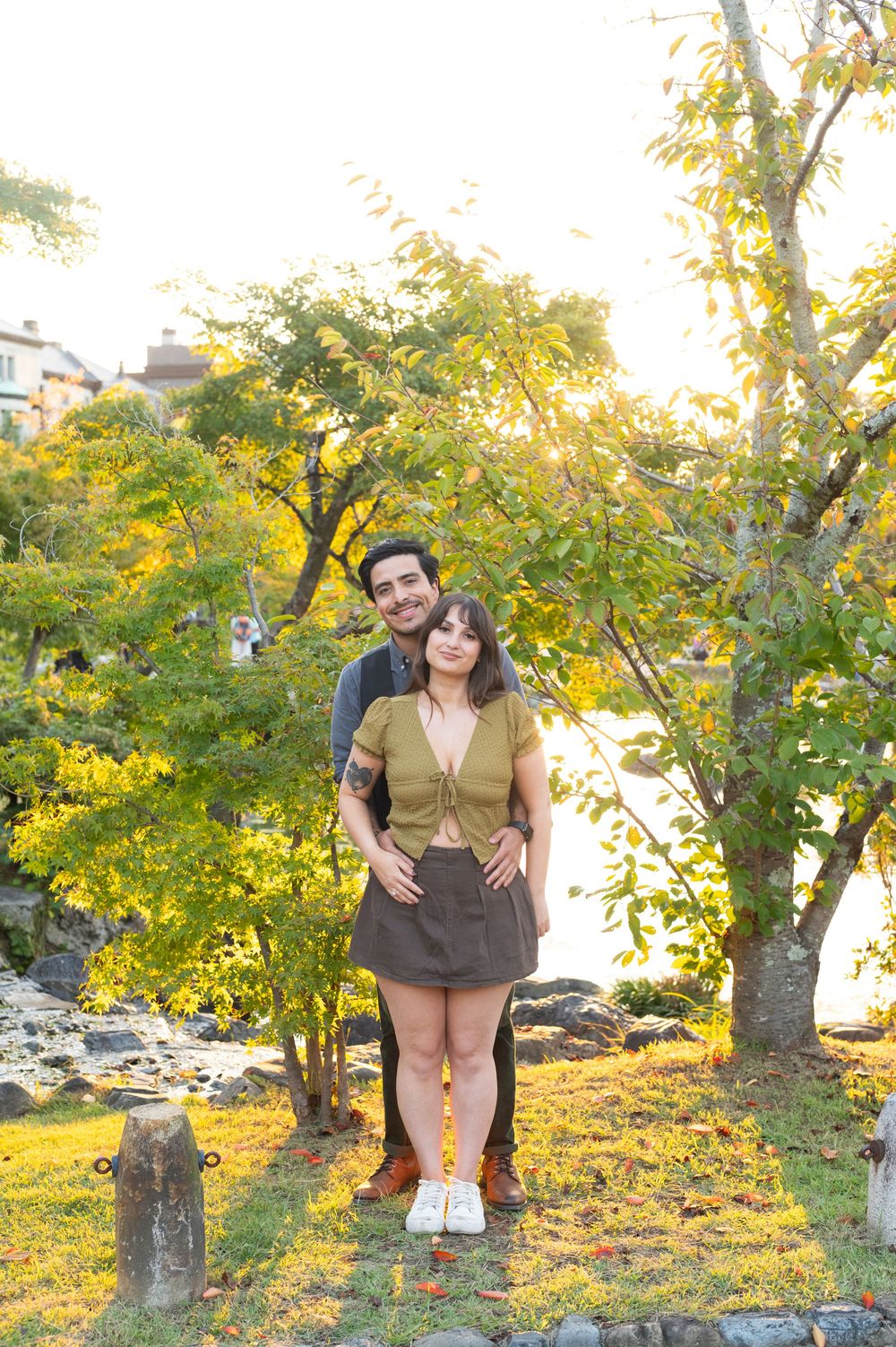 Couple posing together under golden autumn trees by a rocky riverbank in a Japanese garden.
