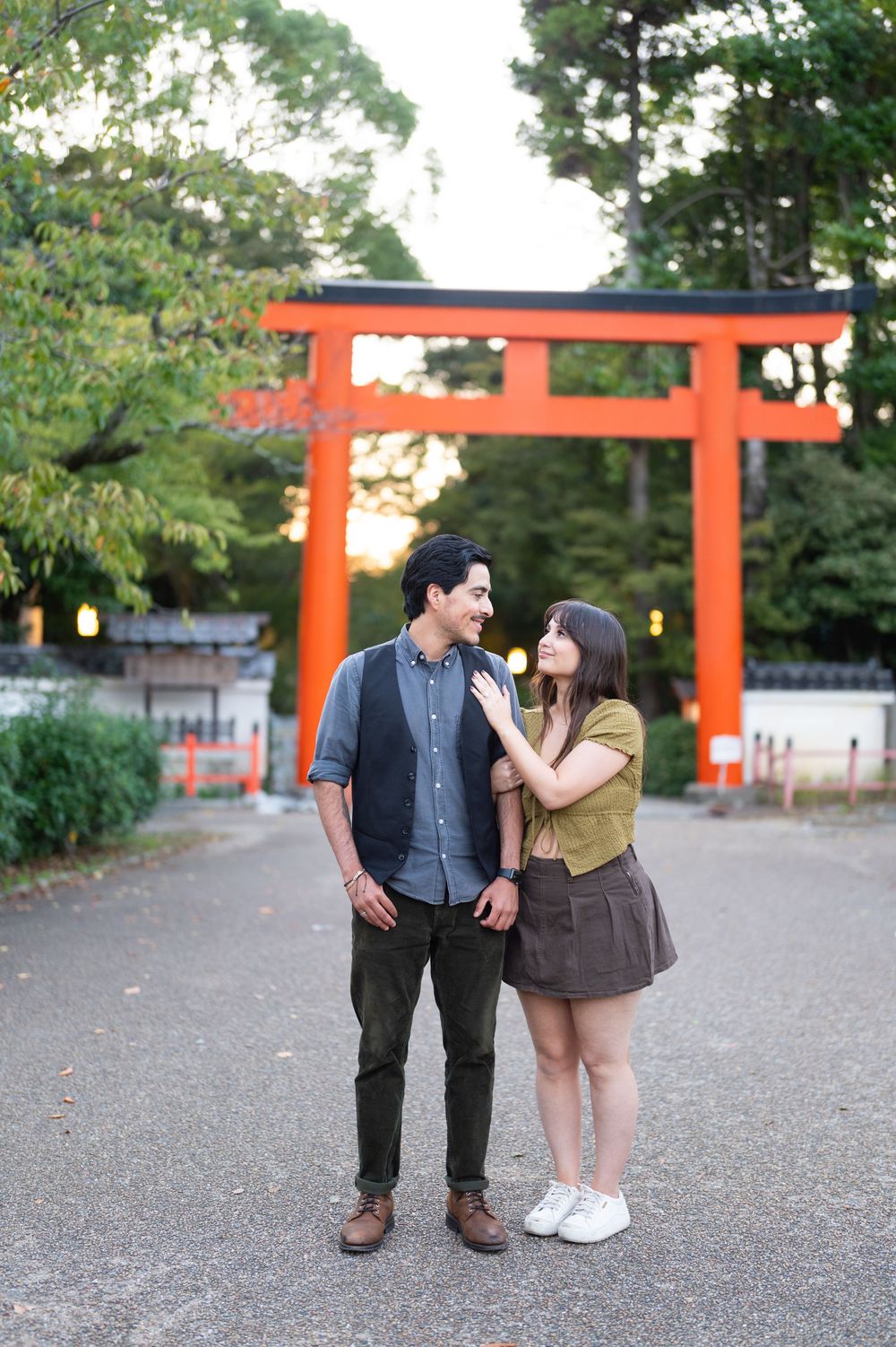 Couple smiling at each other in front of a vibrant red torii gate in a Japanese shrine.