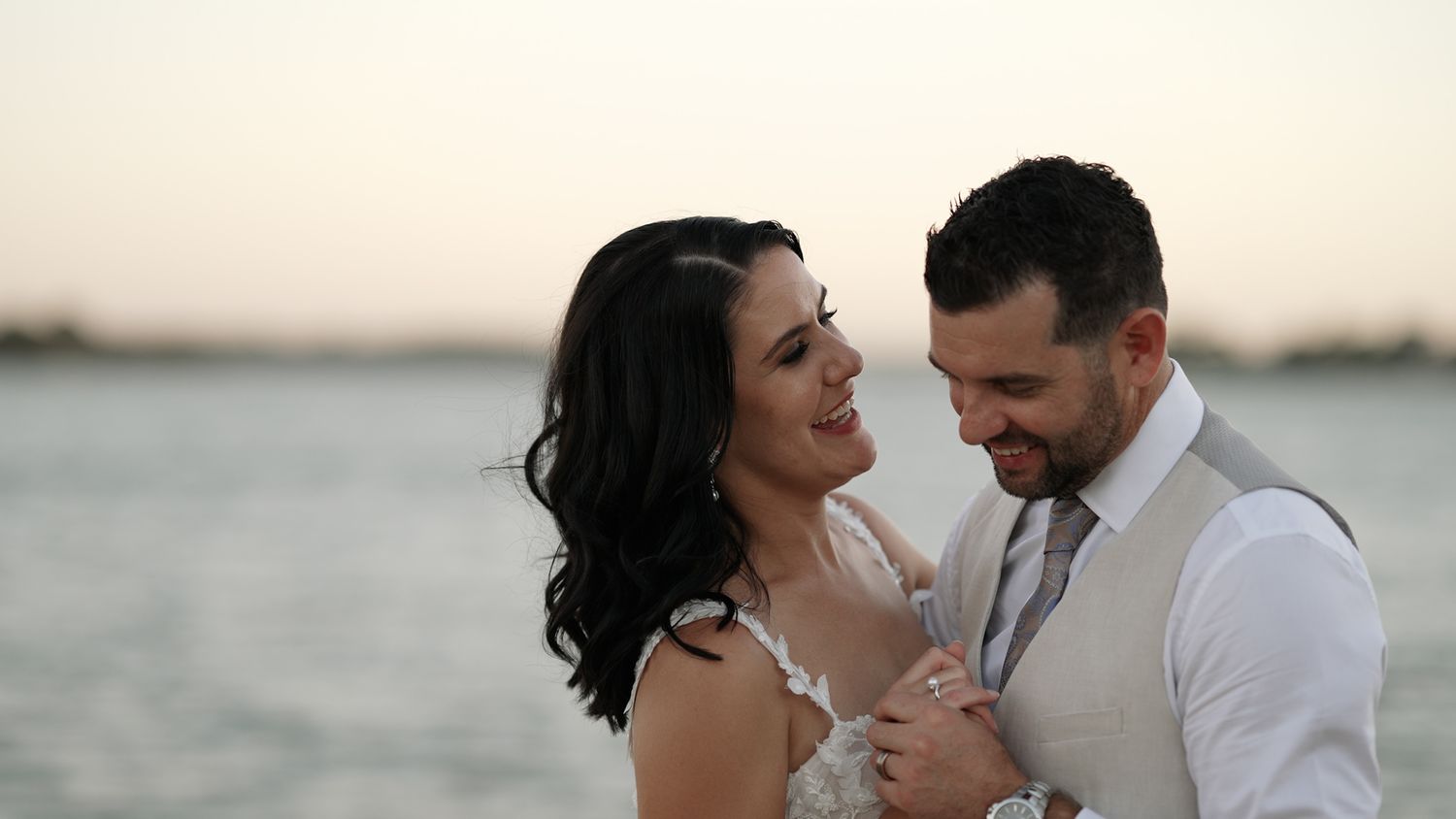 Romantic seaside photoshoot with couple embracing at sunset.