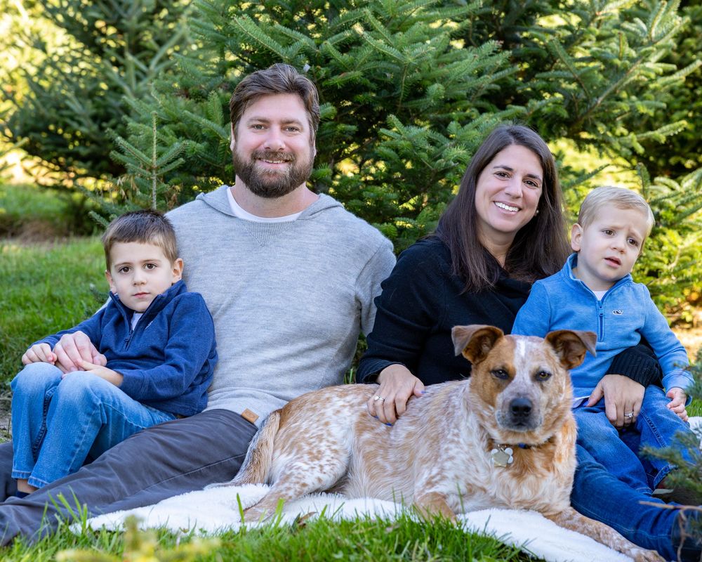 A family poses with trees at Mistletoe Christmas Tree farm in Stow, MA at holiday family photography session by Lisa West Photography.