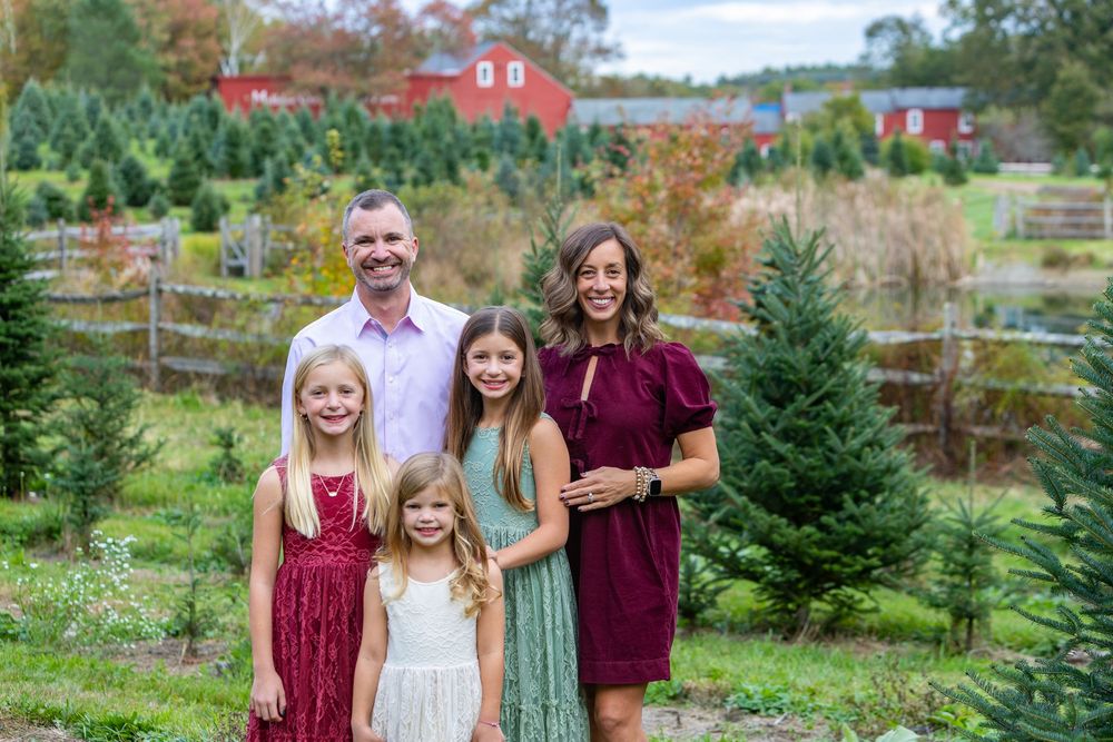 A family poses with trees at Mistletoe Christmas Tree farm in Stow, MA at holiday family photography session by Lisa West Photography.