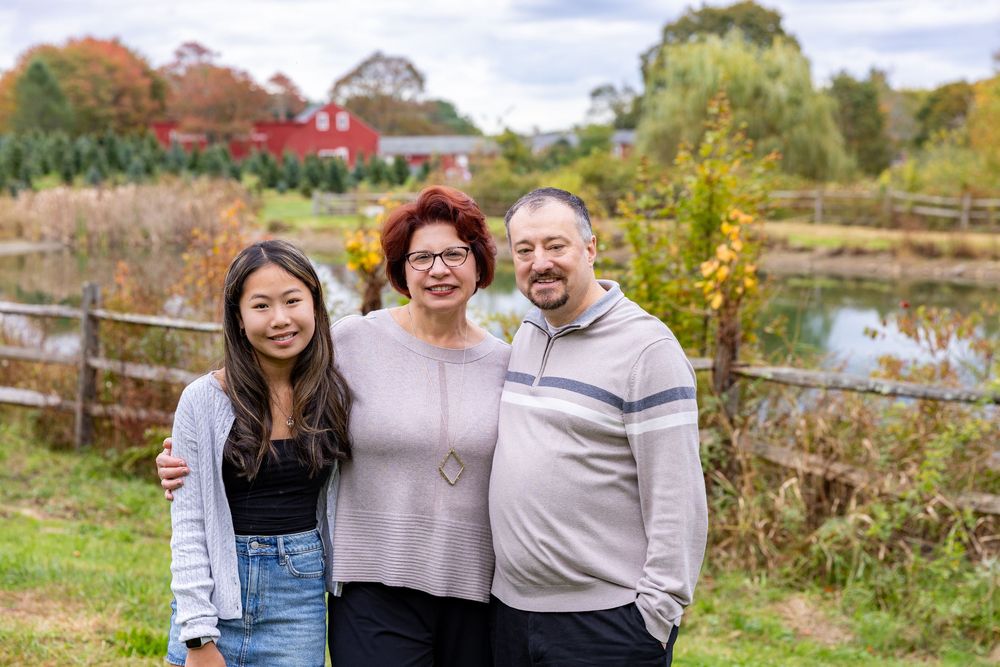 A family poses at a Christmas Tree Farm with red barn in Stow, MA at holiday family photography session by Lisa West Photography.