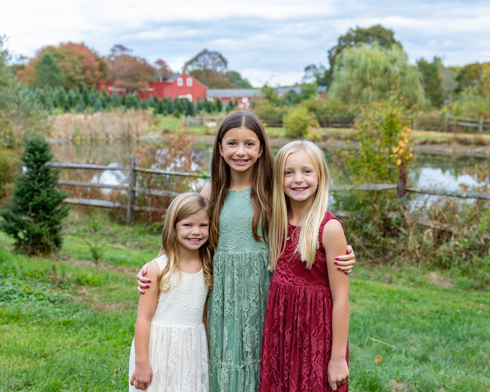 Siblings pose at a Christmas Tree Farm with red barn in Stow, MA at holiday family photography session by Lisa West Photography.