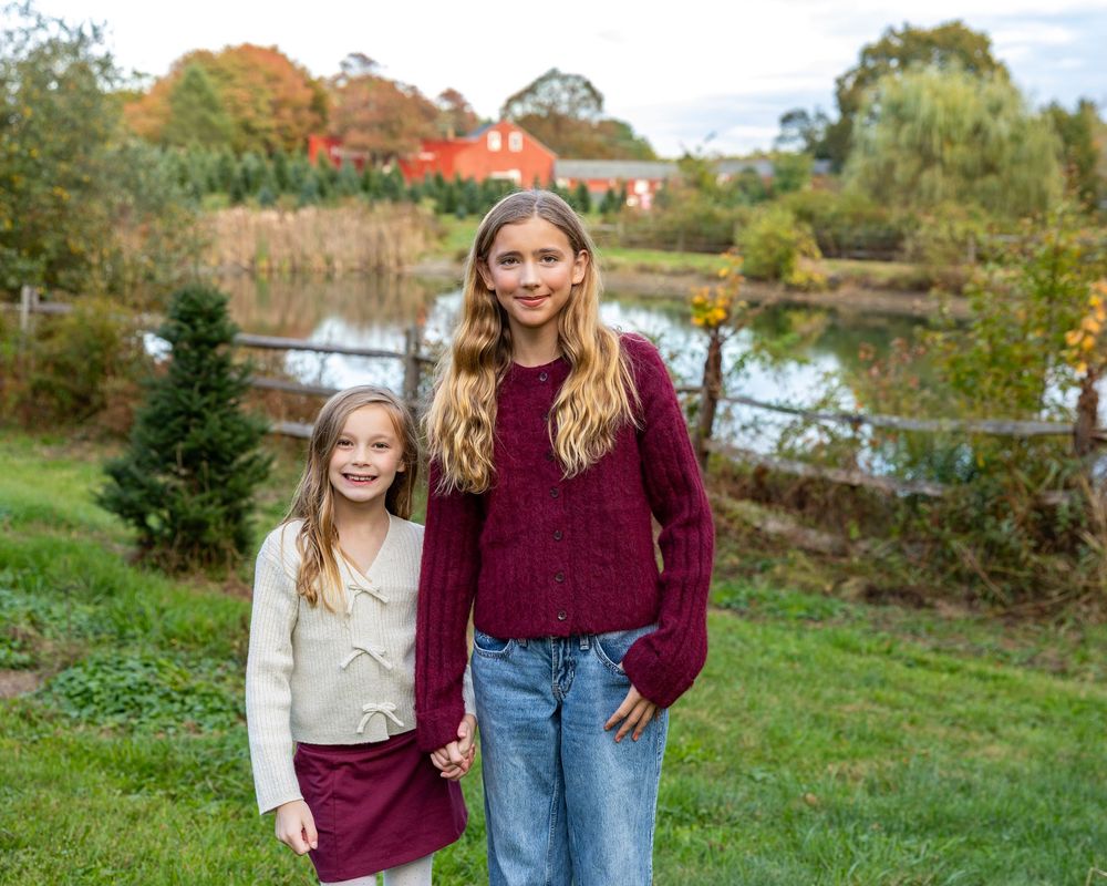 Siblings pose at a Christmas Tree Farm with red barn in Stow, MA at holiday family photography session by Lisa West Photography.