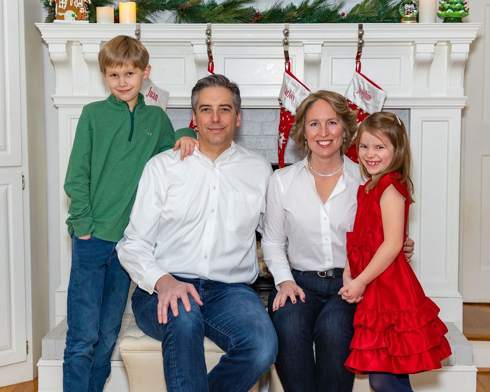 A family poses in front of their decorated mantel during an at home holiday family photo session in Sudbury, MA by Lisa West Photography.