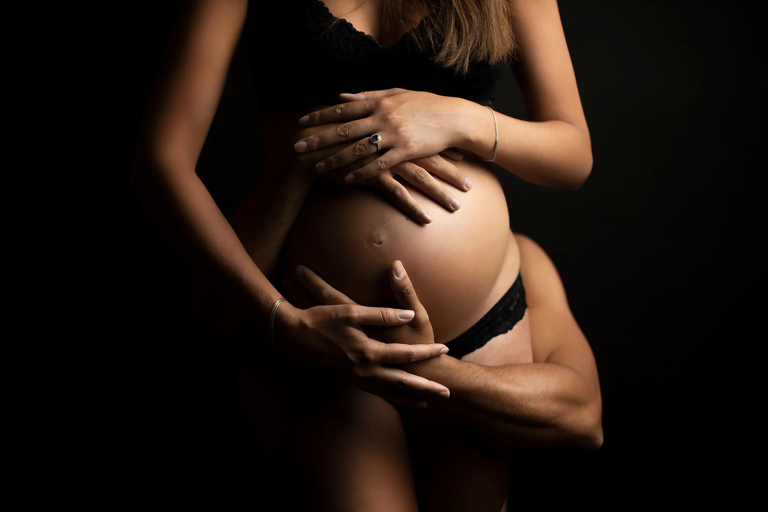 Black and white artistic maternity photo showing a pregnant belly in lace lingerie.