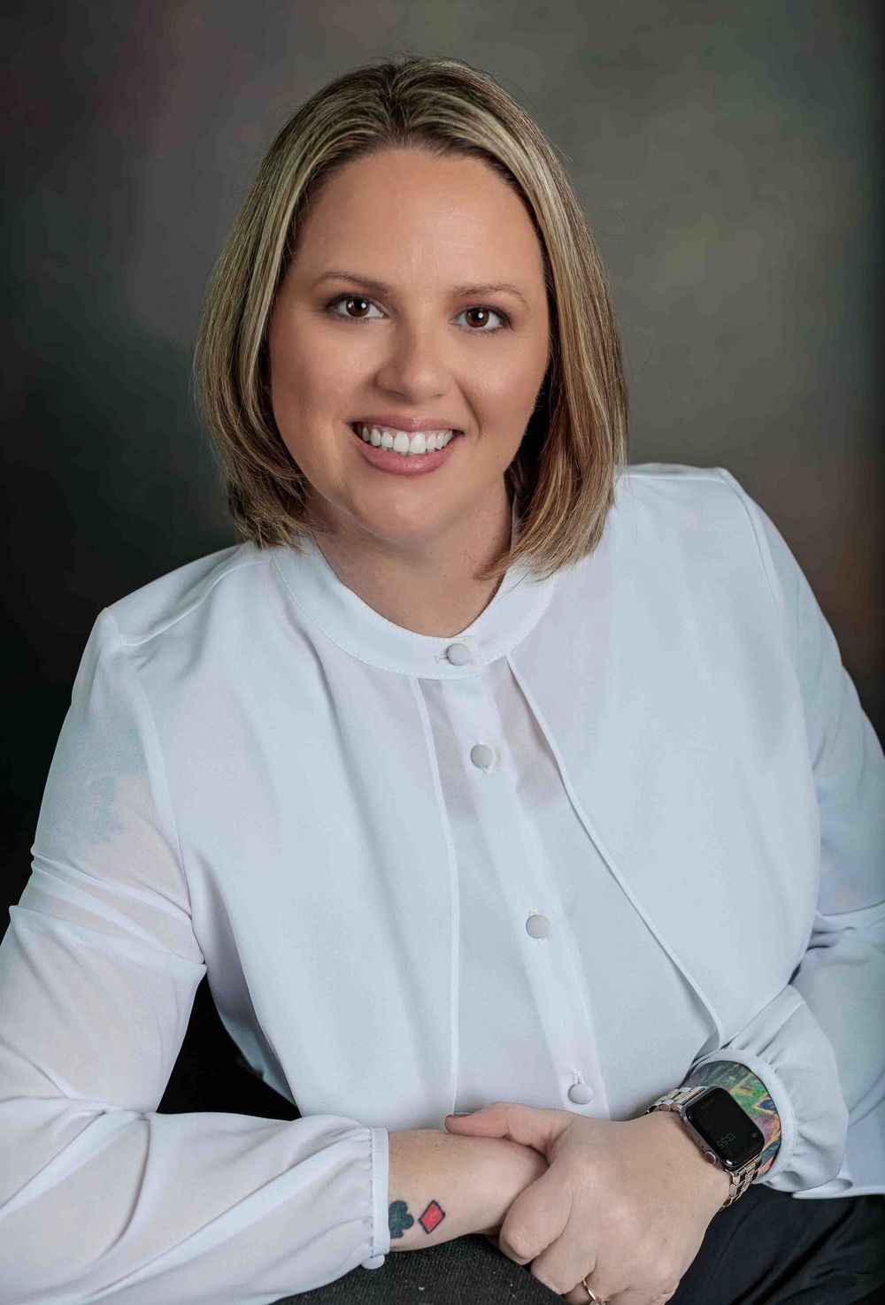 Professional woman with blonde bob smiling in white blouse, formal business headshot portrait.