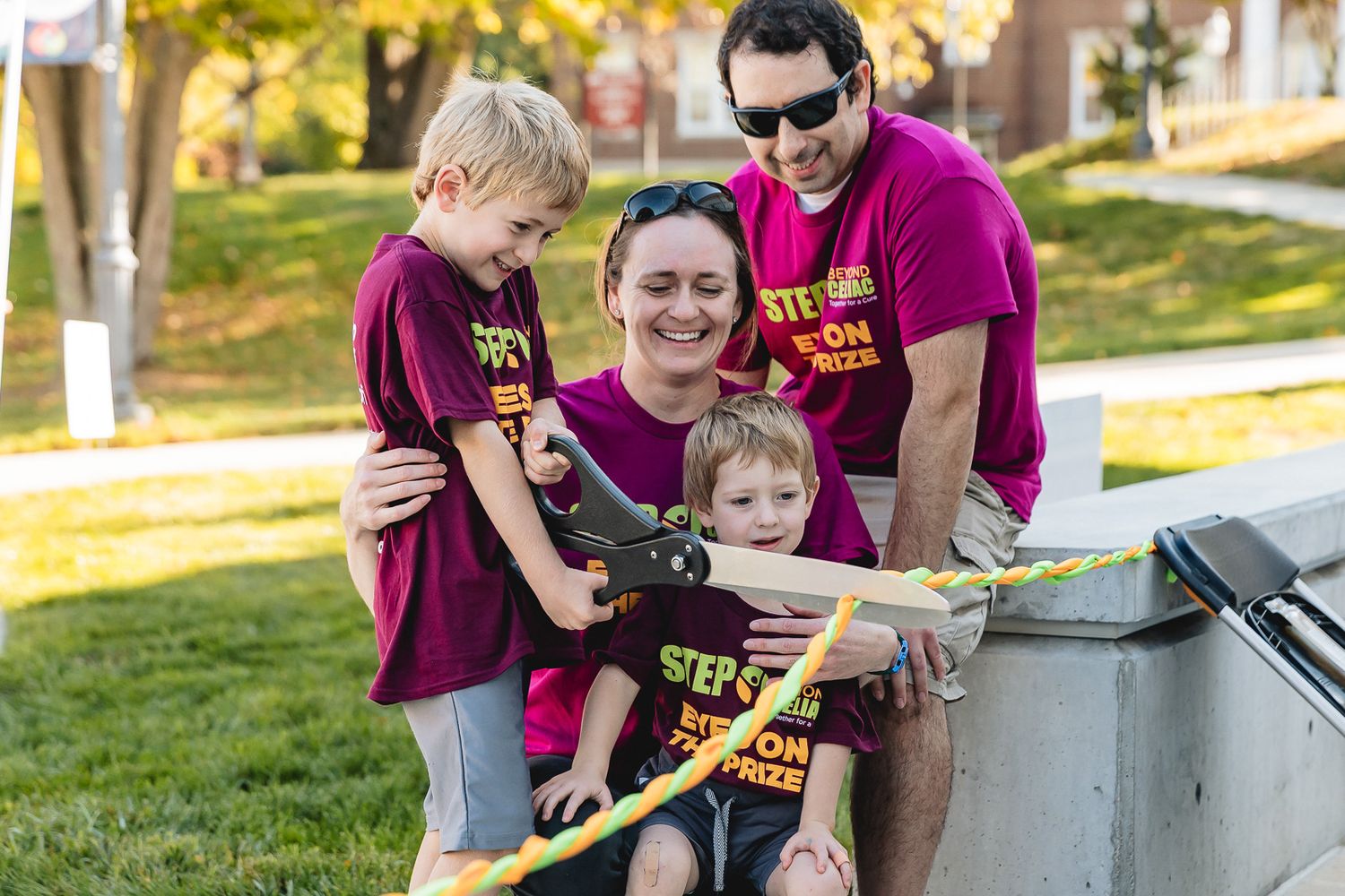 Family in matching purple t-shirts gather around a map while outdoors in a sunny park setting.
