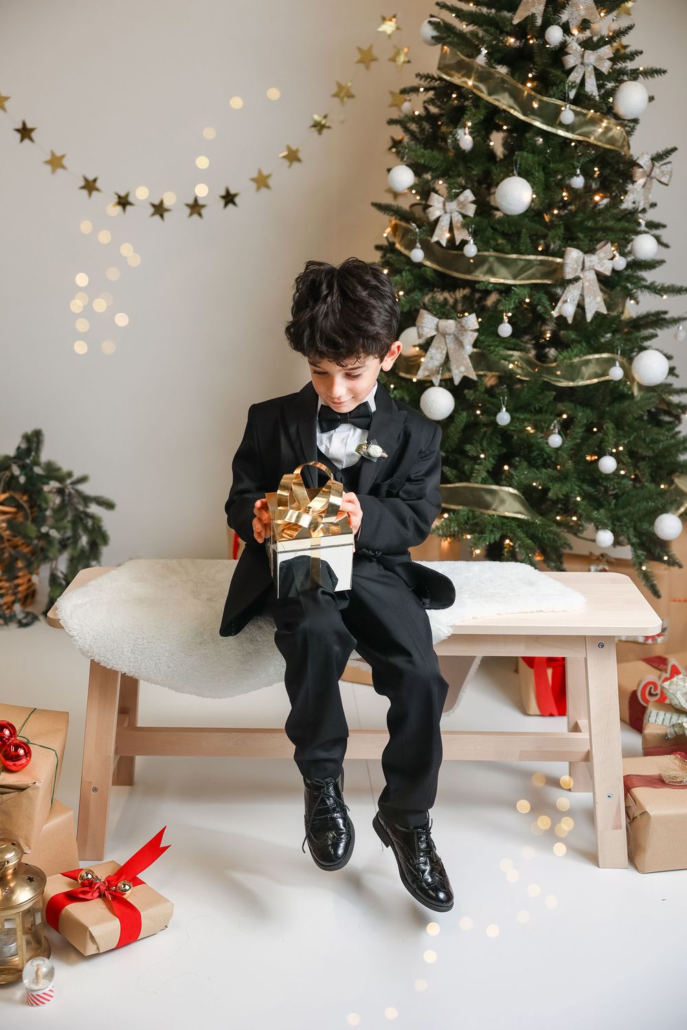 A series of photos showing a child in a black suit sitting by a Christmas tree opening presents and enjoying holiday treats.
