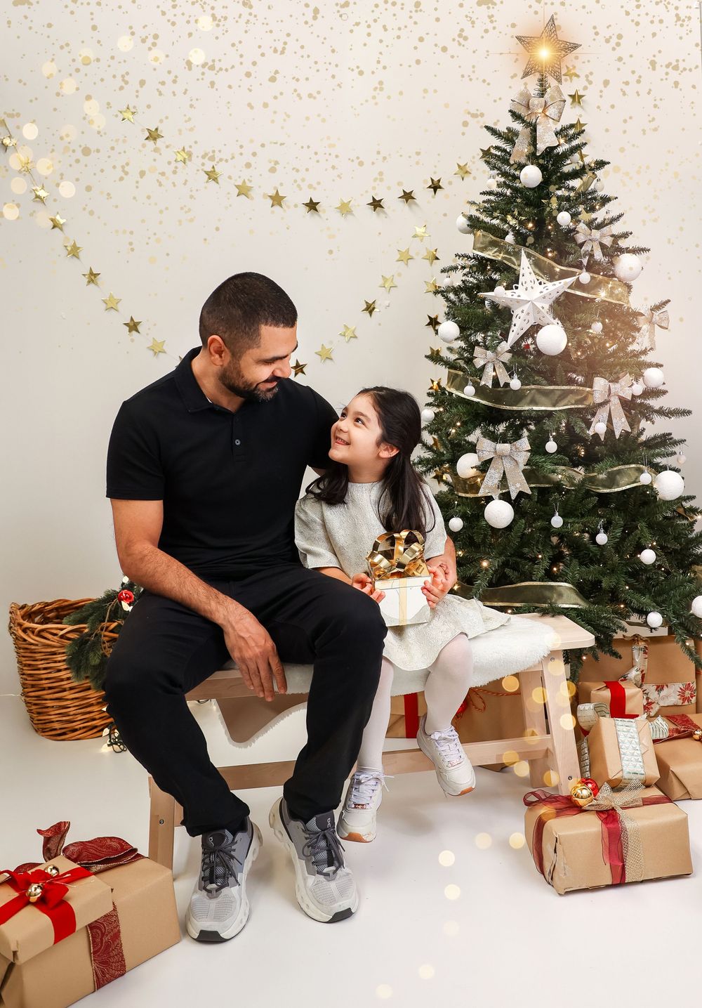 Romantic couple sits together by a decorated Christmas tree with wrapped presents and star decorations.