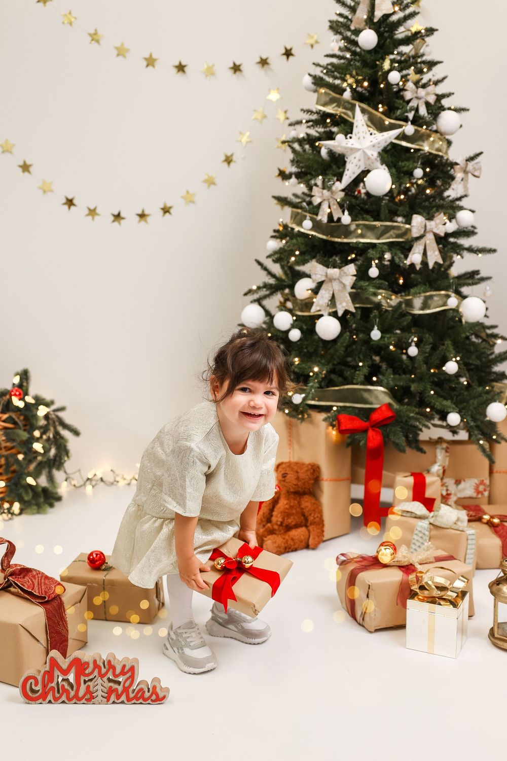 Christmas presents and decorations arranged under a decorated evergreen tree with star garland and white bows.