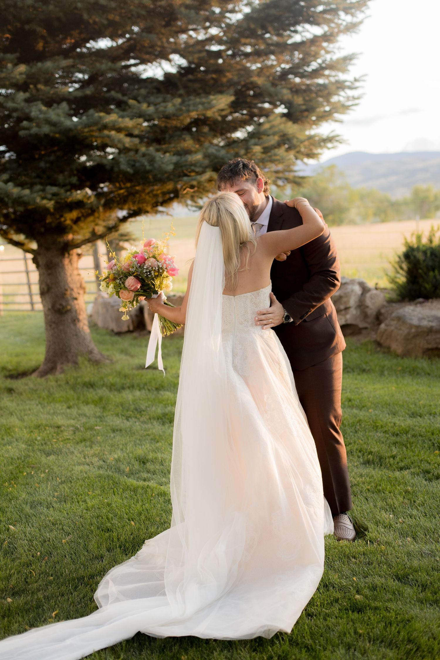 A romantic wedding moment captured outdoors with a flowing white dress and veil against a scenic mountain backdrop.