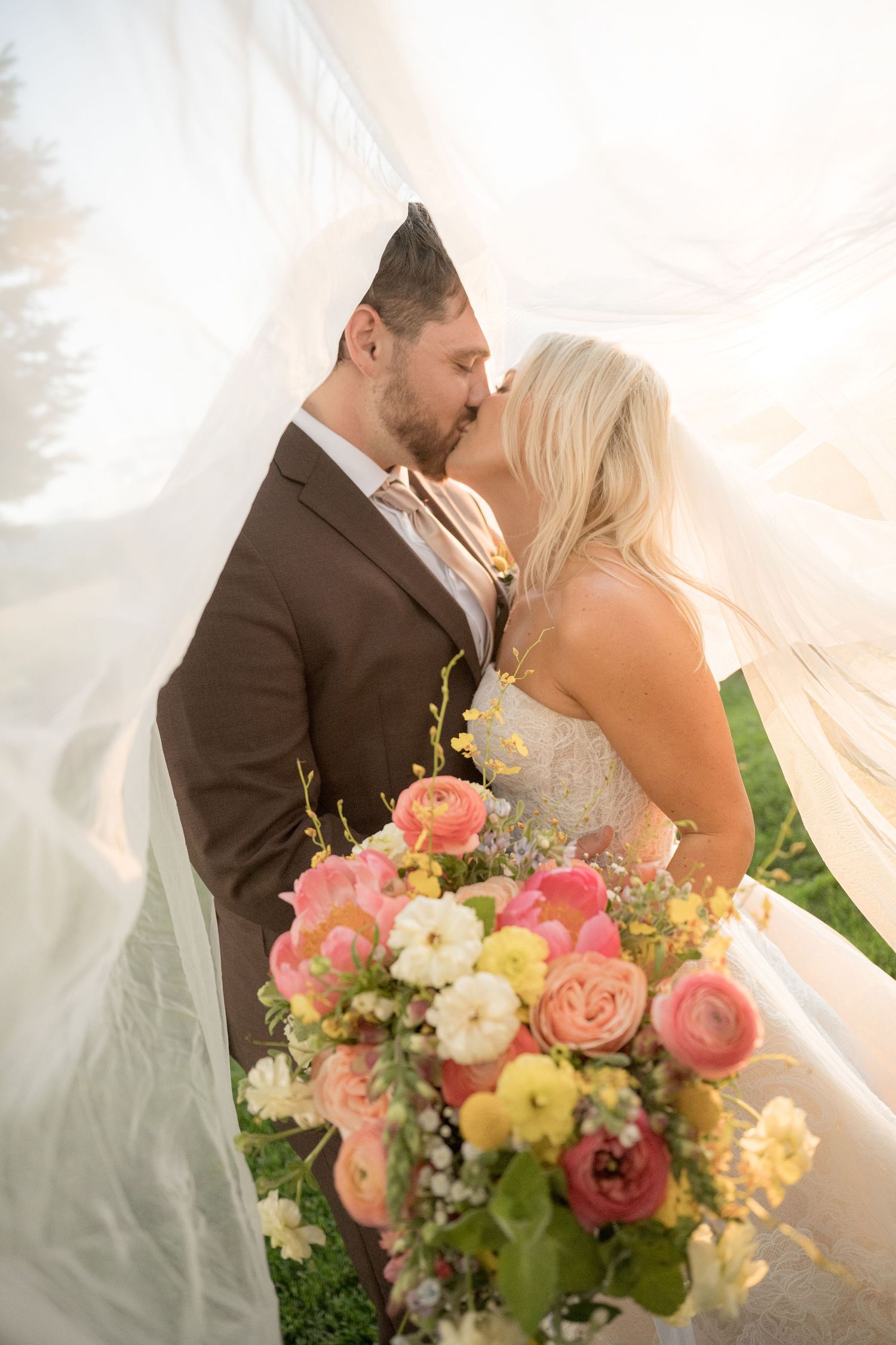 A dreamy wedding scene with soft veil blowing in the wind and colorful coral and peach floral bouquet.