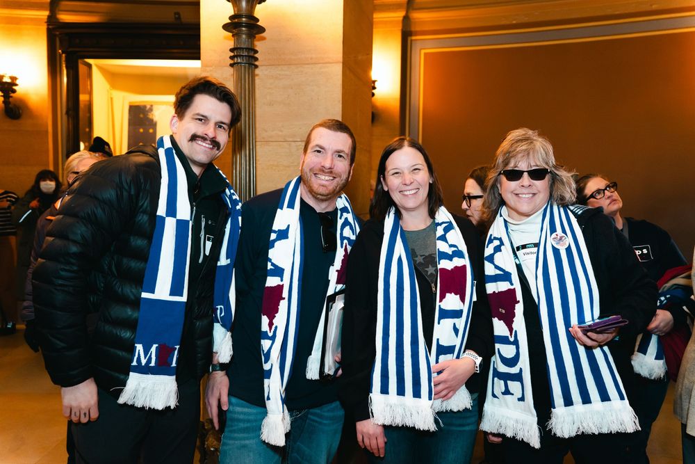 Soccer fans wearing black and white striped scarves gather in an indoor venue with warm lighting.