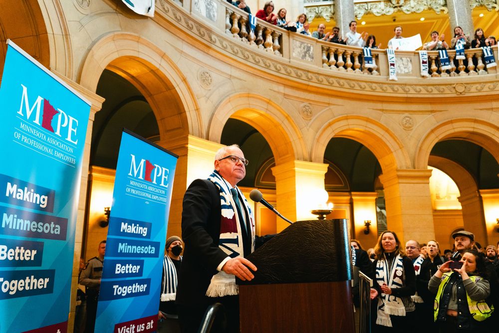 A large ornate rotunda with arched architecture and blue banners displaying text, filled with spectators on multiple levels.