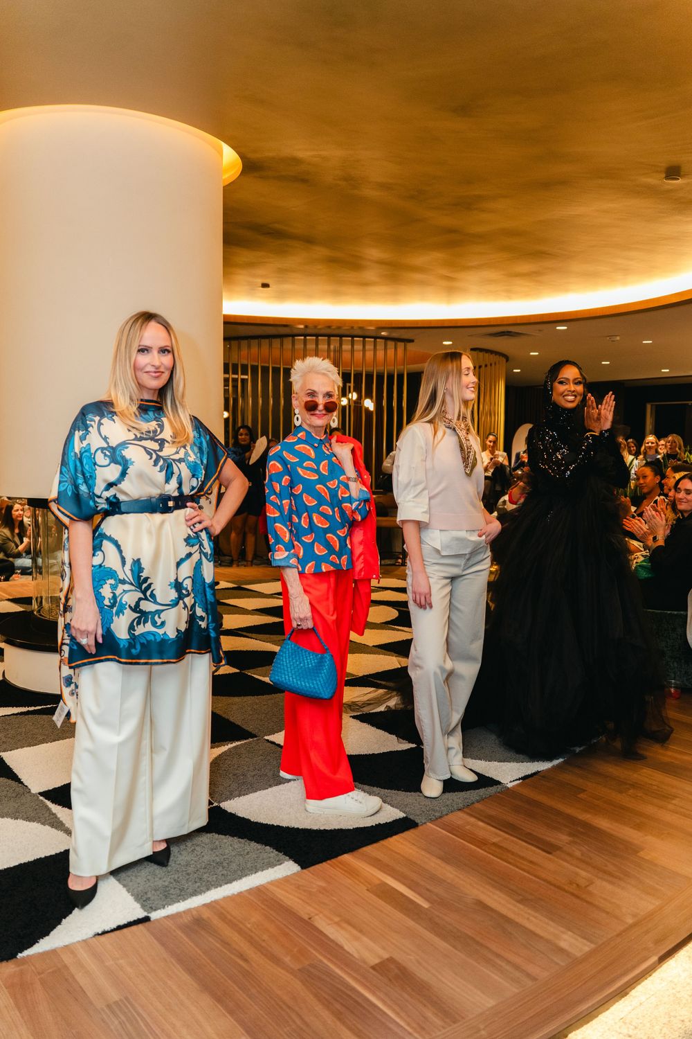 People gather in a modern venue with wood flooring and curved white walls at an indoor social event.