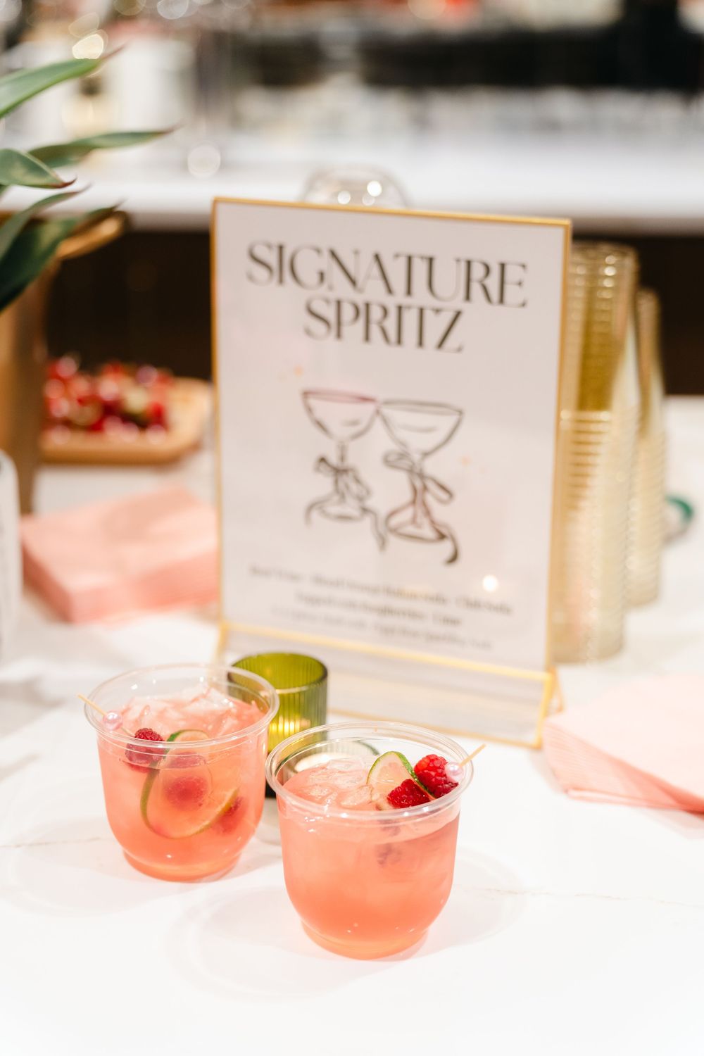 Two pink cocktails with fresh raspberries served next to a 'Signature Spritz' menu sign on a table setting.