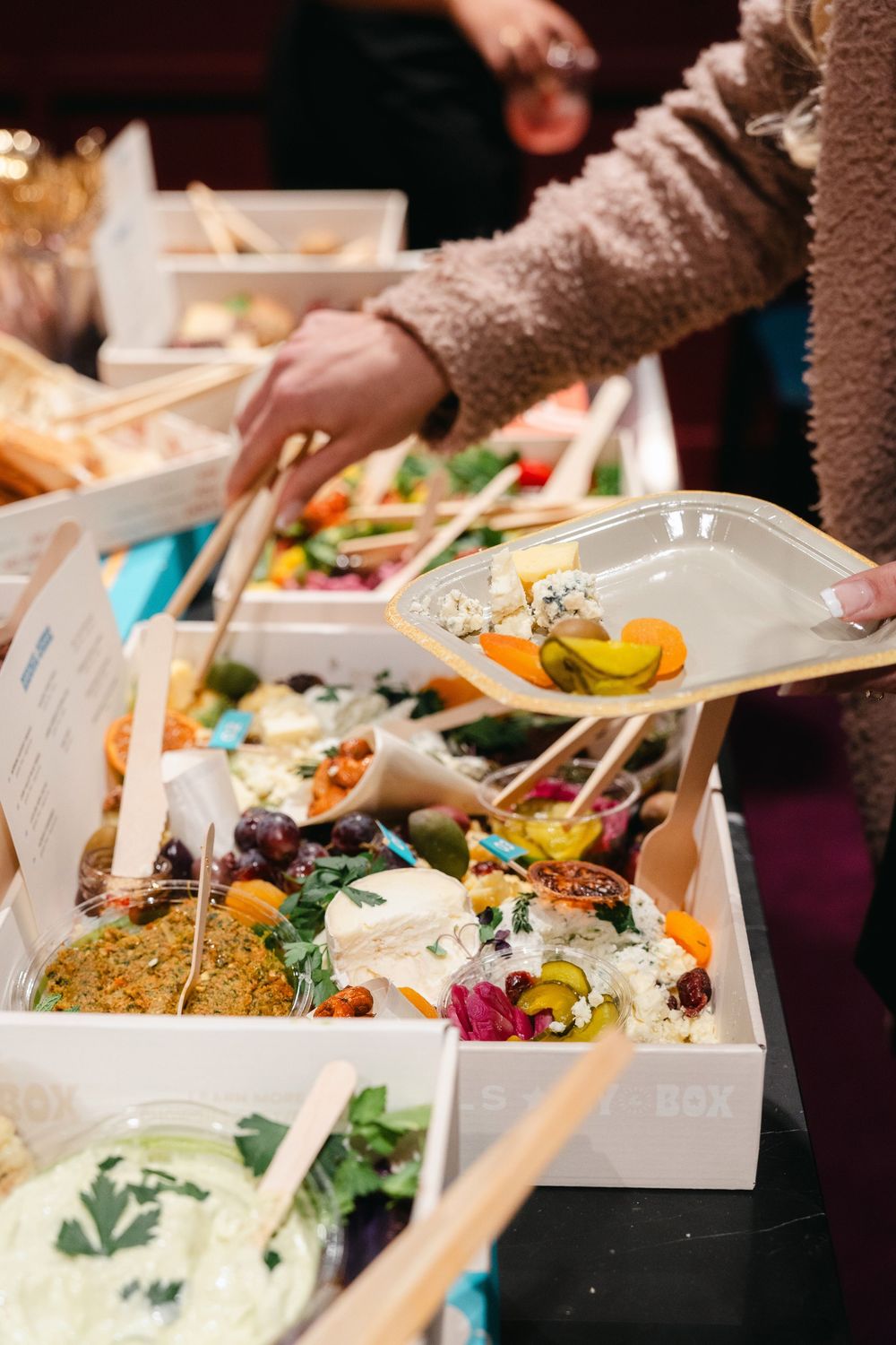 People serving themselves food from white takeout containers at a buffet style meal service.