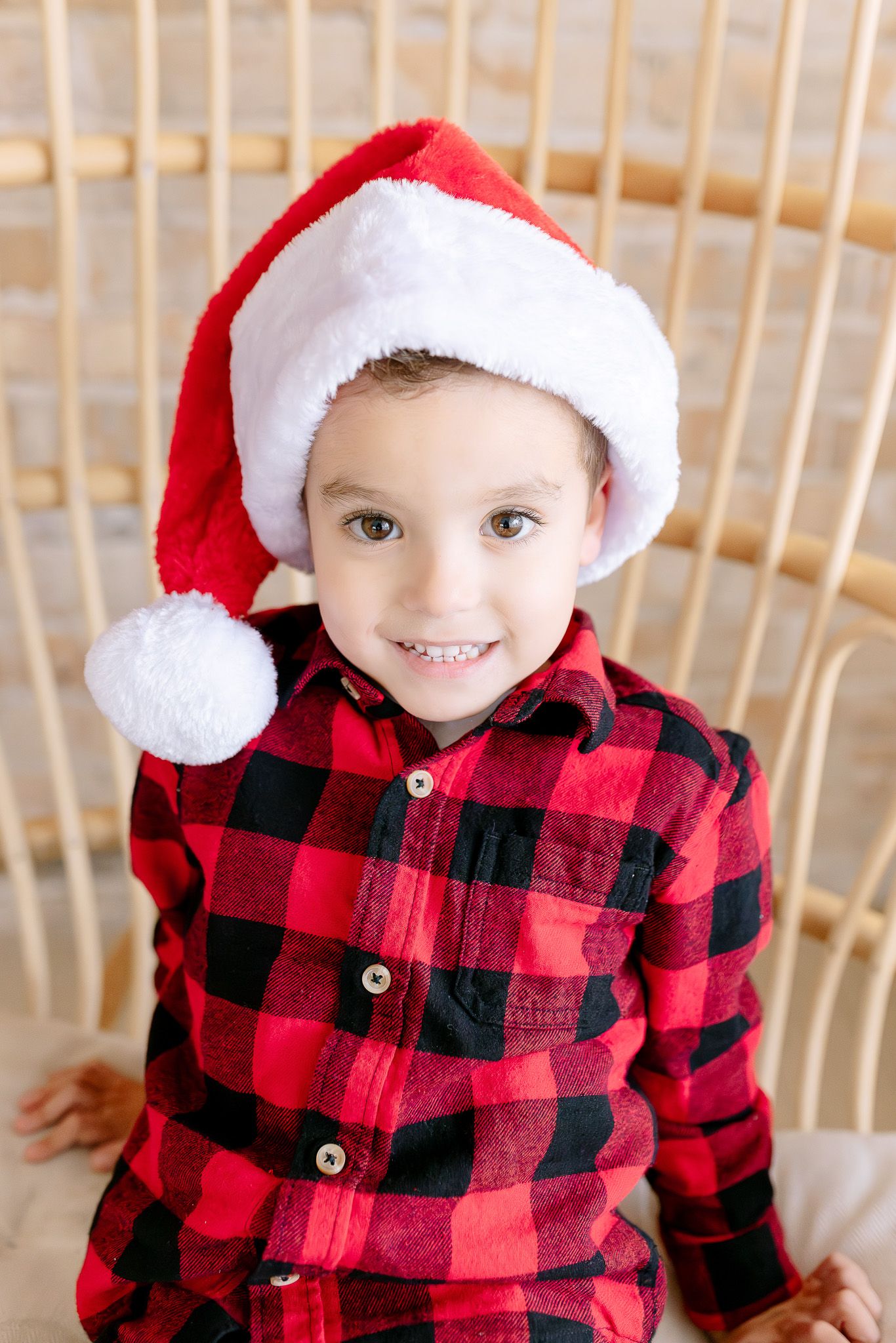 Children wearing matching red and black buffalo plaid shirts and white Santa hats pose together during holiday season.
