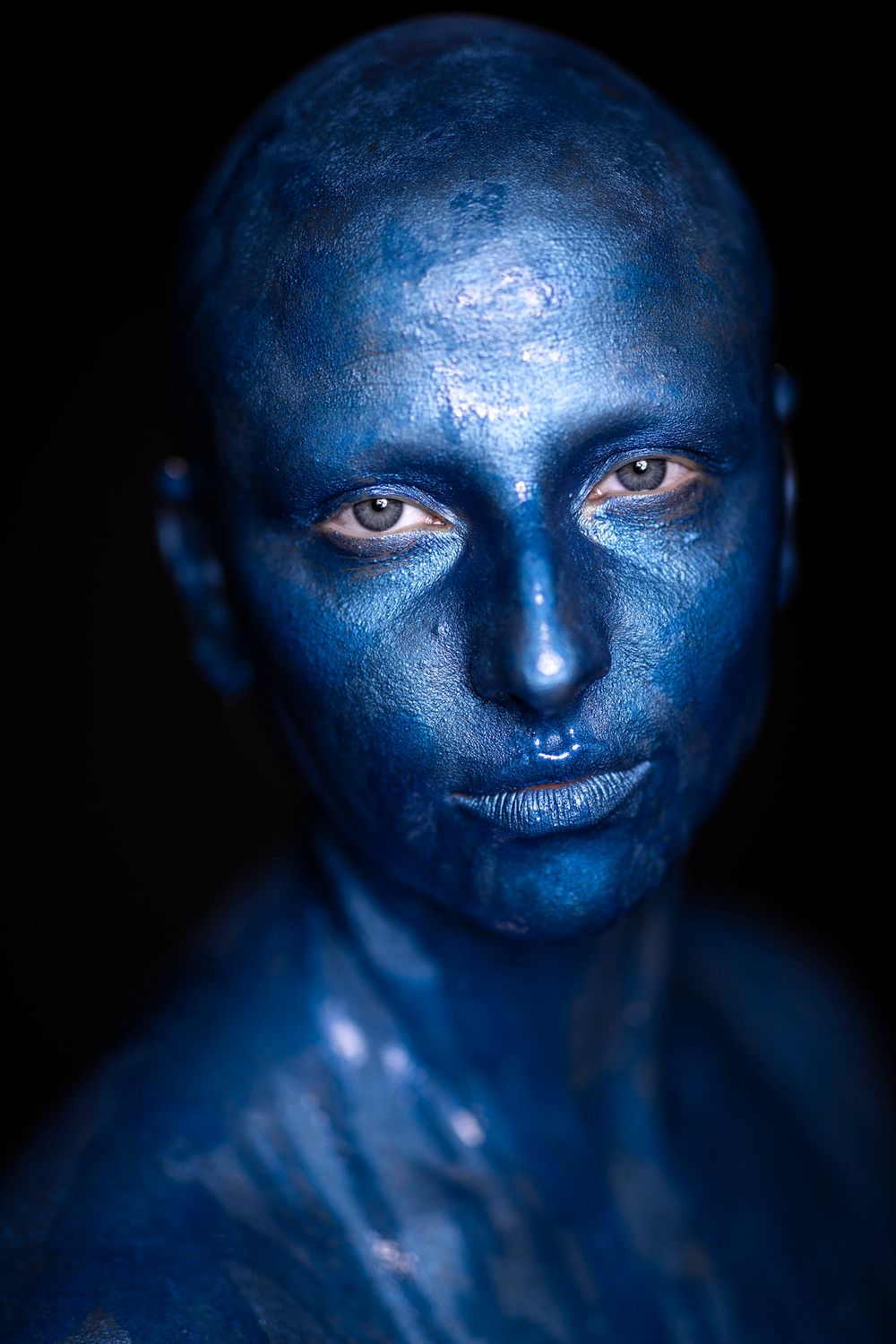 Close-up portraits of face painted in metallic blue makeup with intense gaze.