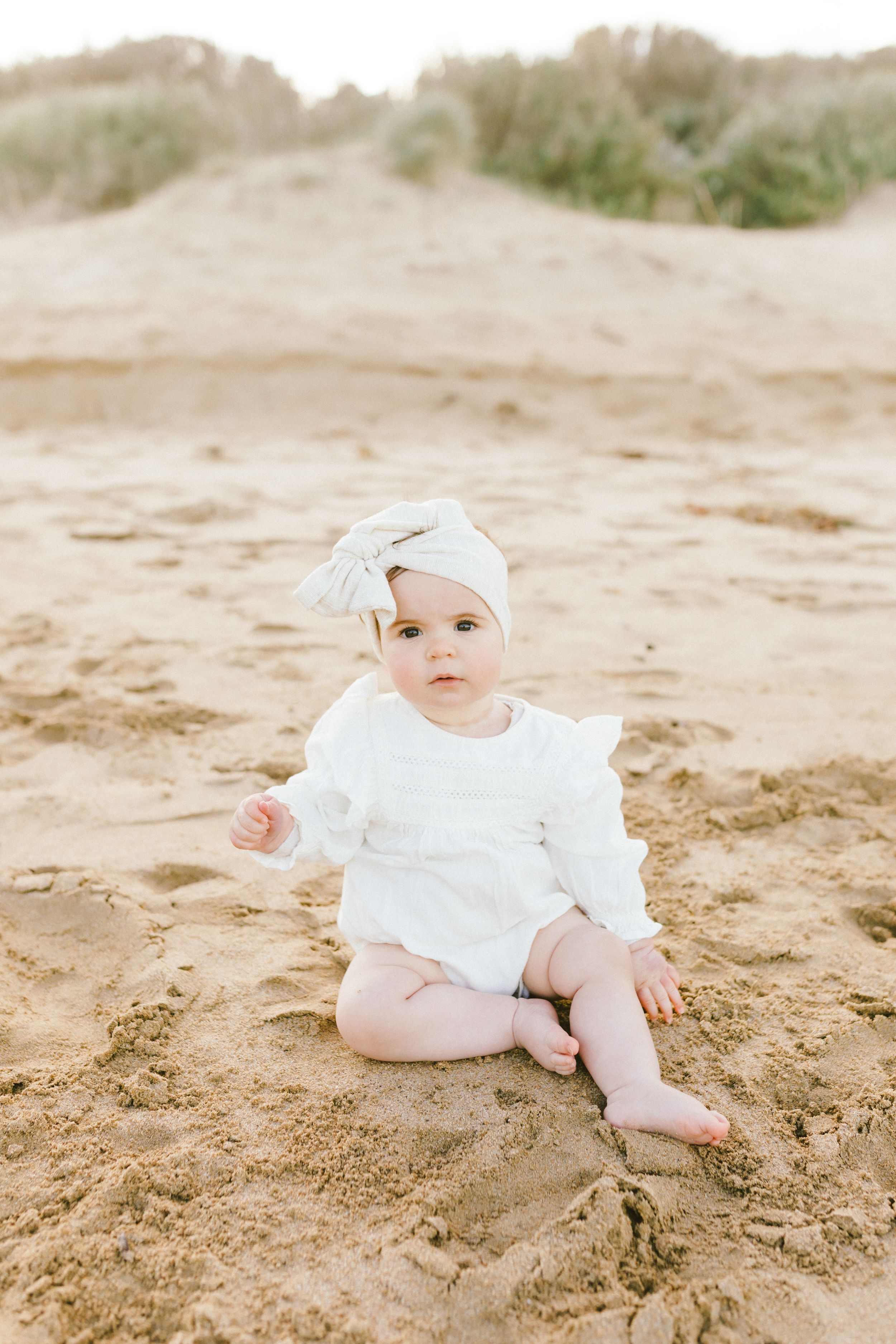 A baby in white clothing lies on sandy beach in a series of connected photos showing different poses.