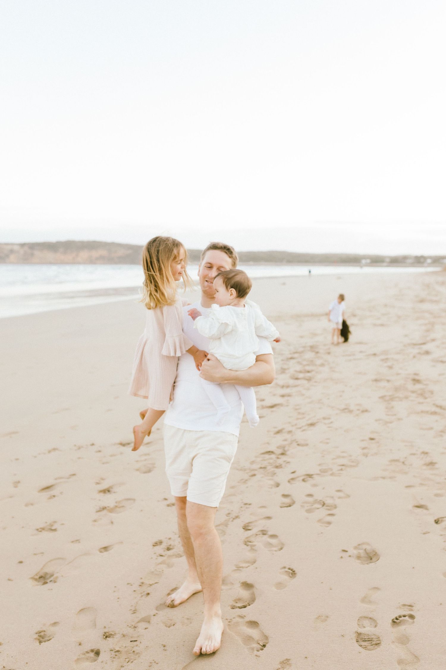 A couple in white outfits dancing and twirling together on a sandy beach at sunset.