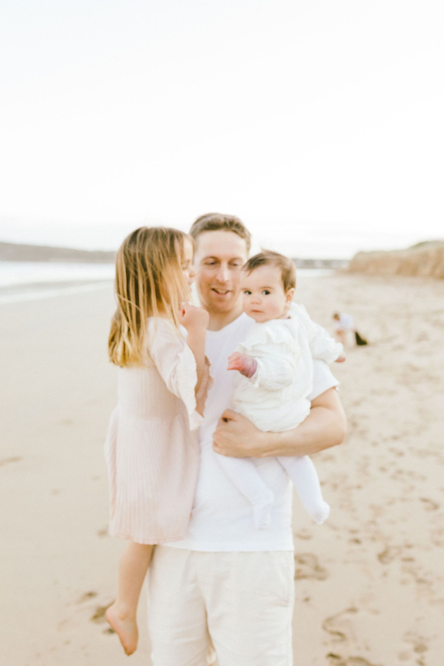 A tender family moment captured at sunset on a peaceful beach with soft lighting and coastal scenery.