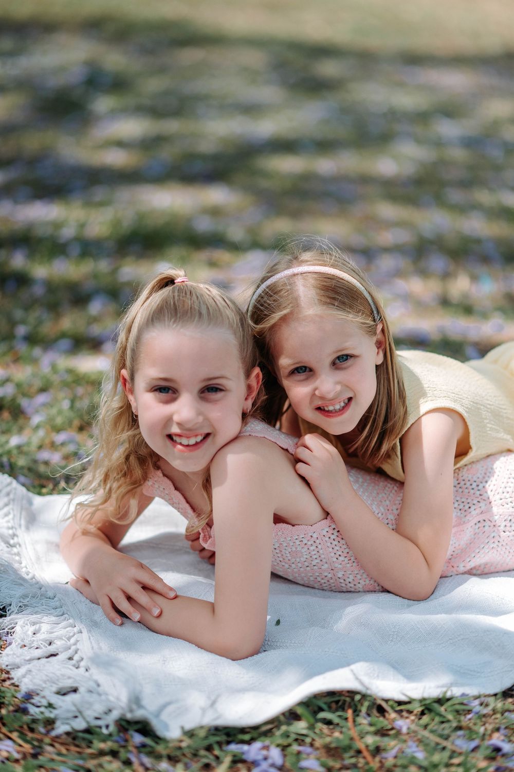 Two children lying on a white blanket outdoors sharing playful moments together.