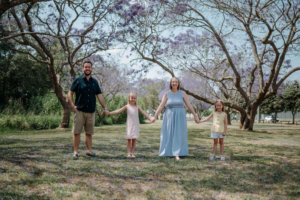 People enjoying a spring day under purple jacaranda trees in a scenic outdoor setting.