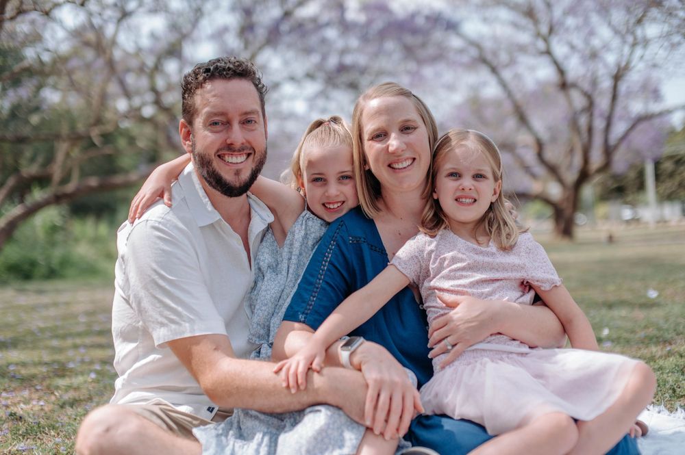 A family sits together on a blanket in a park during springtime with blooming trees in the background.