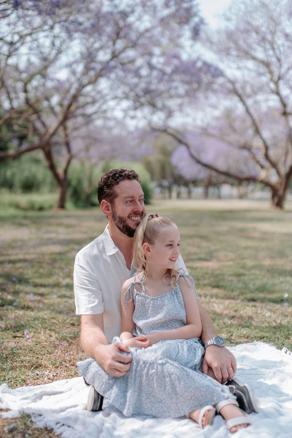 A tender moment captured on a picnic blanket under blooming cherry blossom trees in a peaceful park setting.