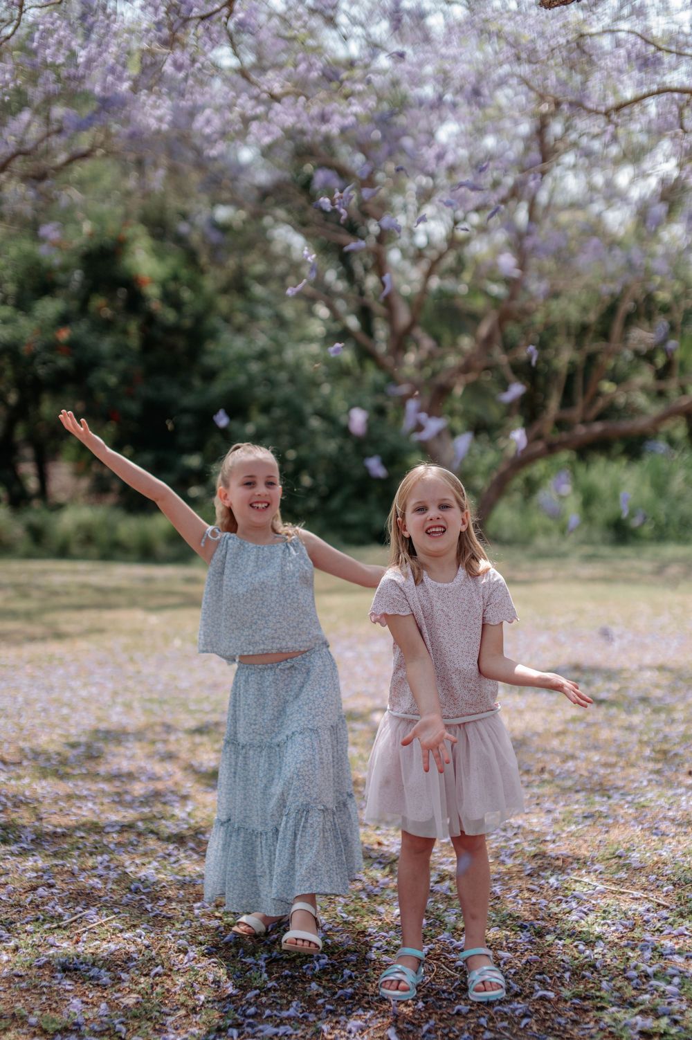 Two young children playing and dancing together under blooming cherry blossom trees on a spring day.