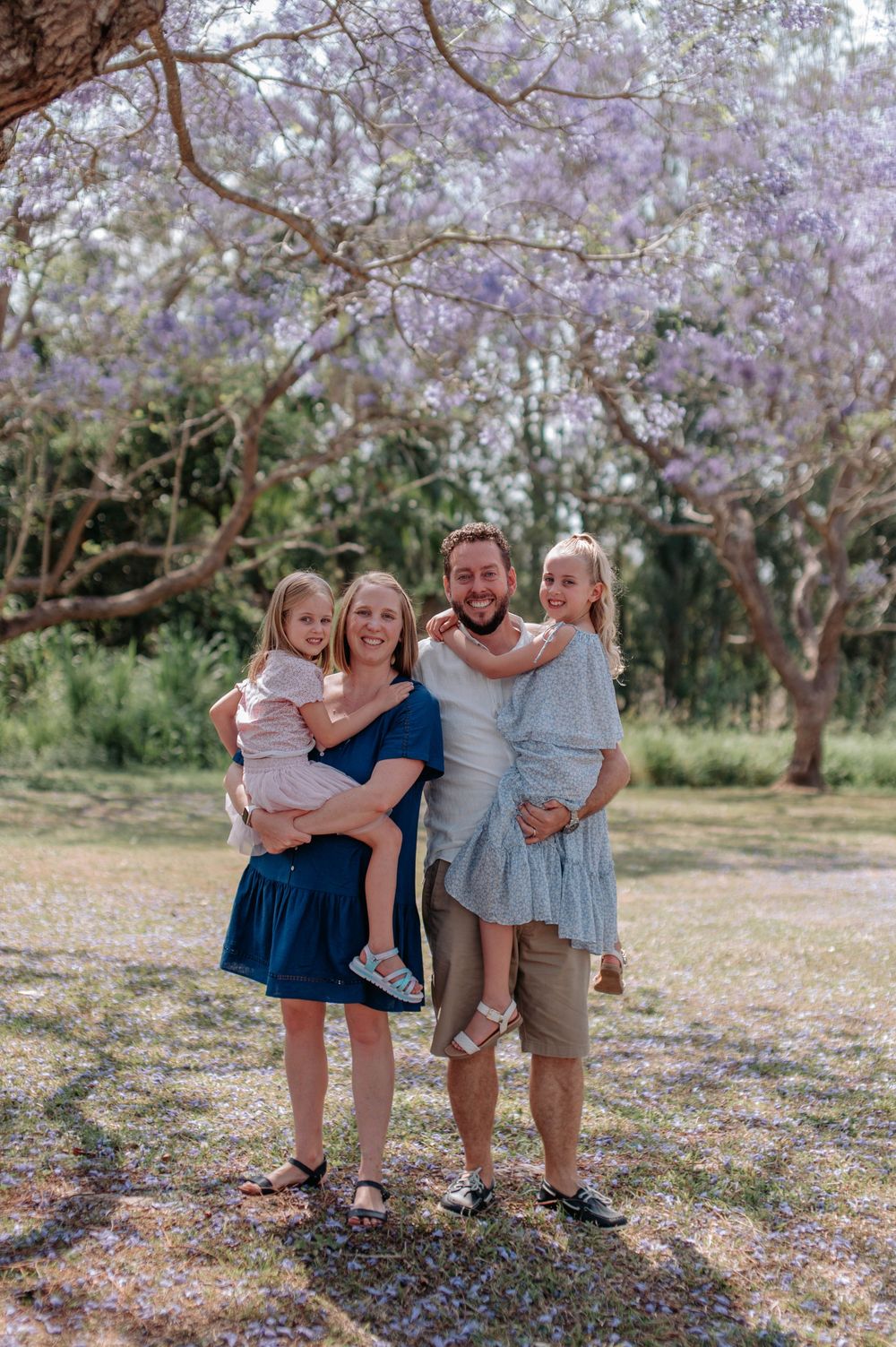 Family enjoying a sunny day together under blooming jacaranda trees in a park.