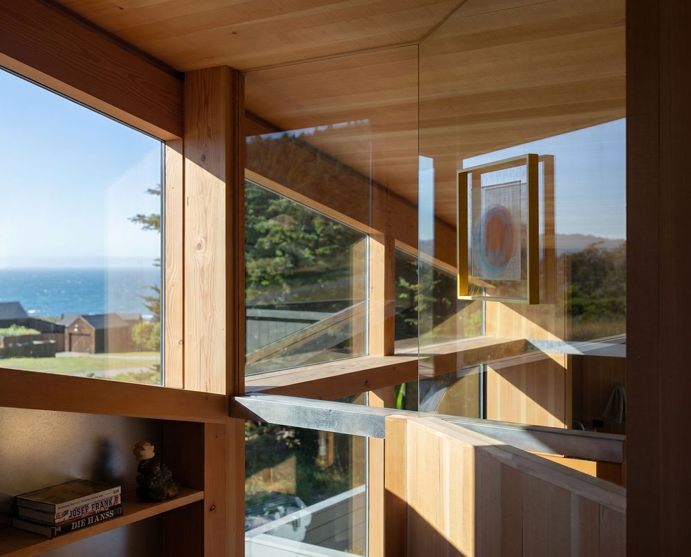 Interior wood-framed windows with ocean view, open casement panels, and built-in shelving in a modern coastal home.