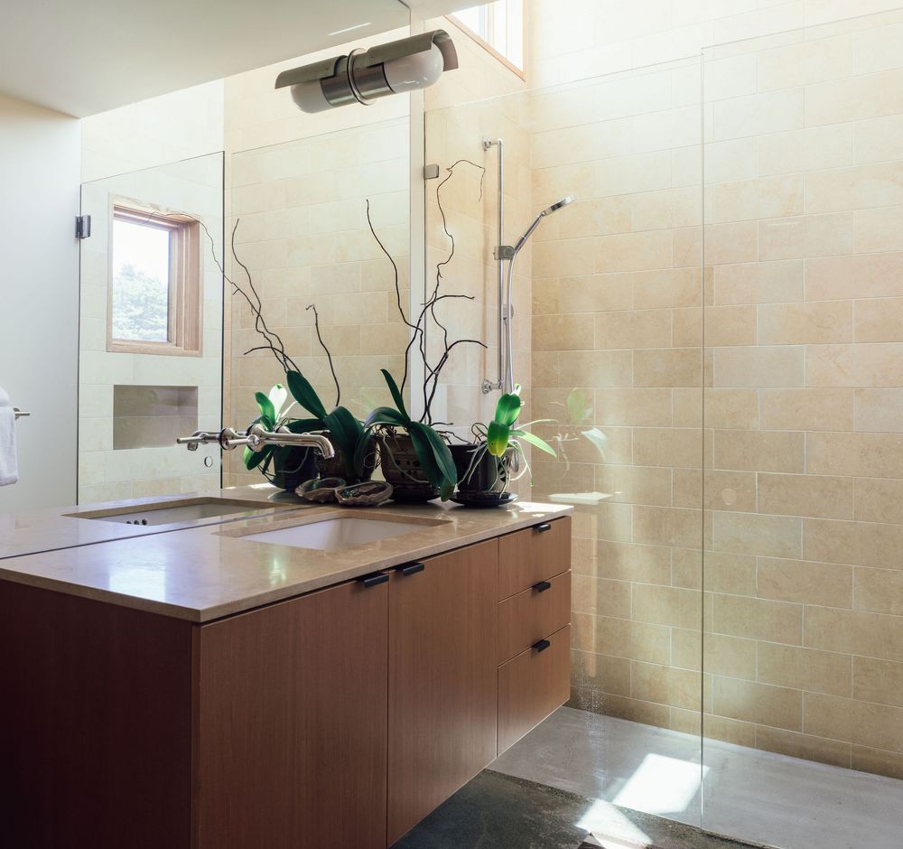 Modern bathroom with wood vanity, large mirror, orchid plants, walk-in shower, and natural stone tile walls.