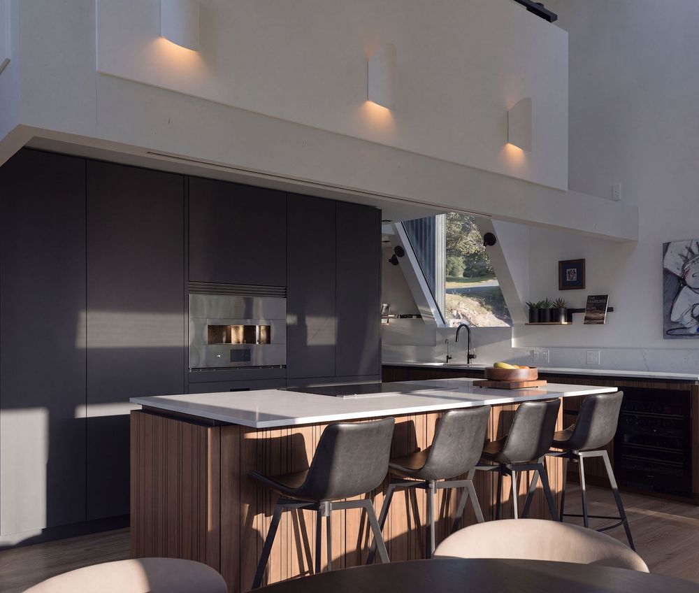 Contemporary kitchen featuring dark cabinetry, wood-paneled island with bar stools, high ceilings, and a unique angled skylight window.