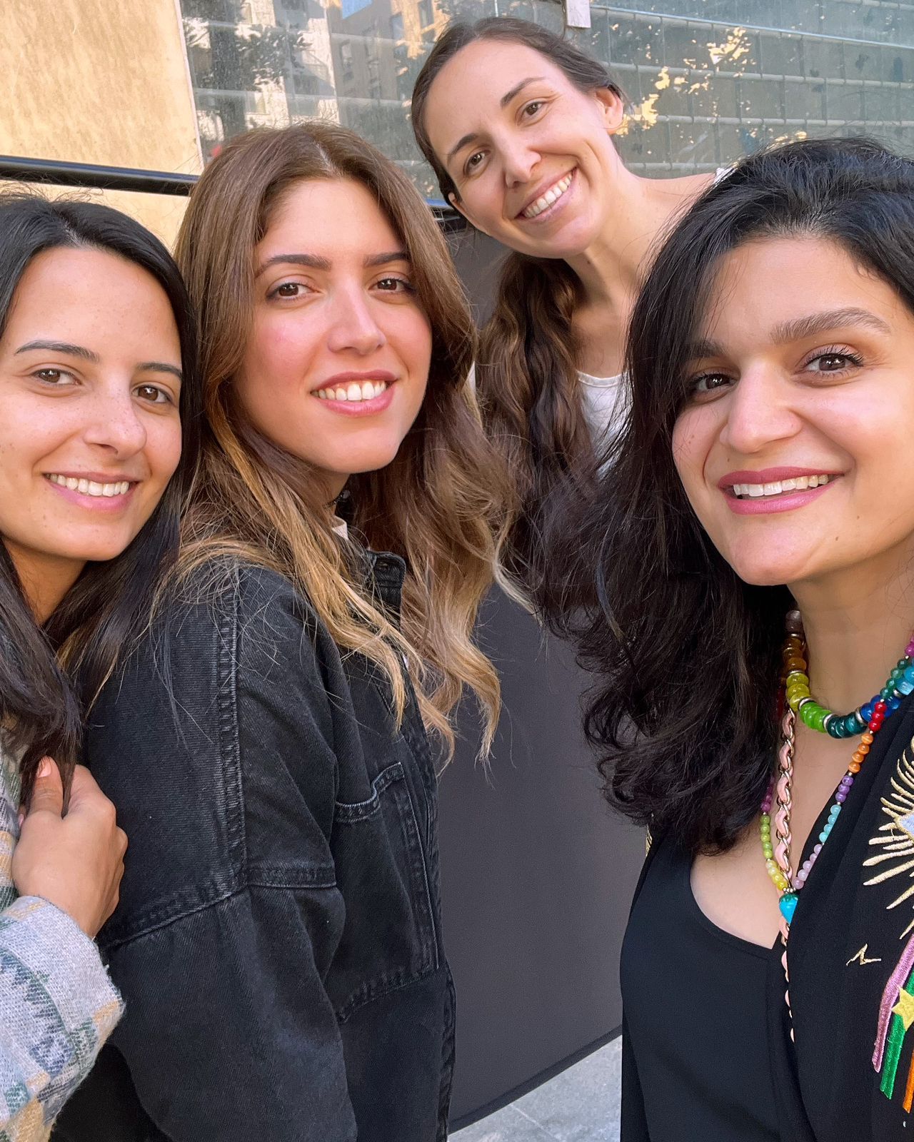 A group of friends in dark clothing smile together while taking a selfie outdoors.