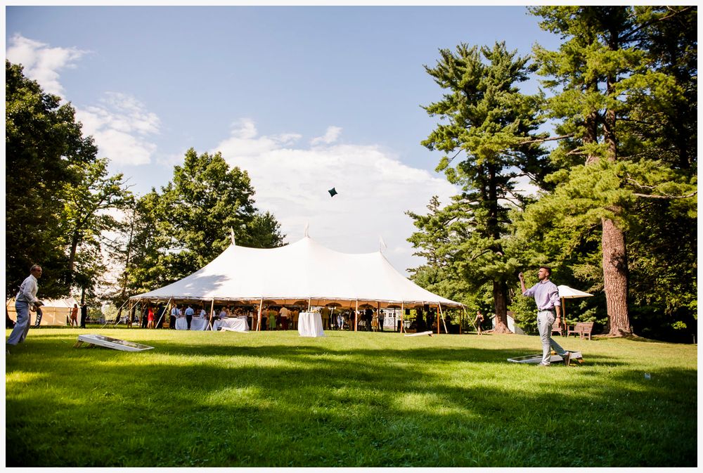 Large white event tent set up on grassy lawn surrounded by tall pine trees.