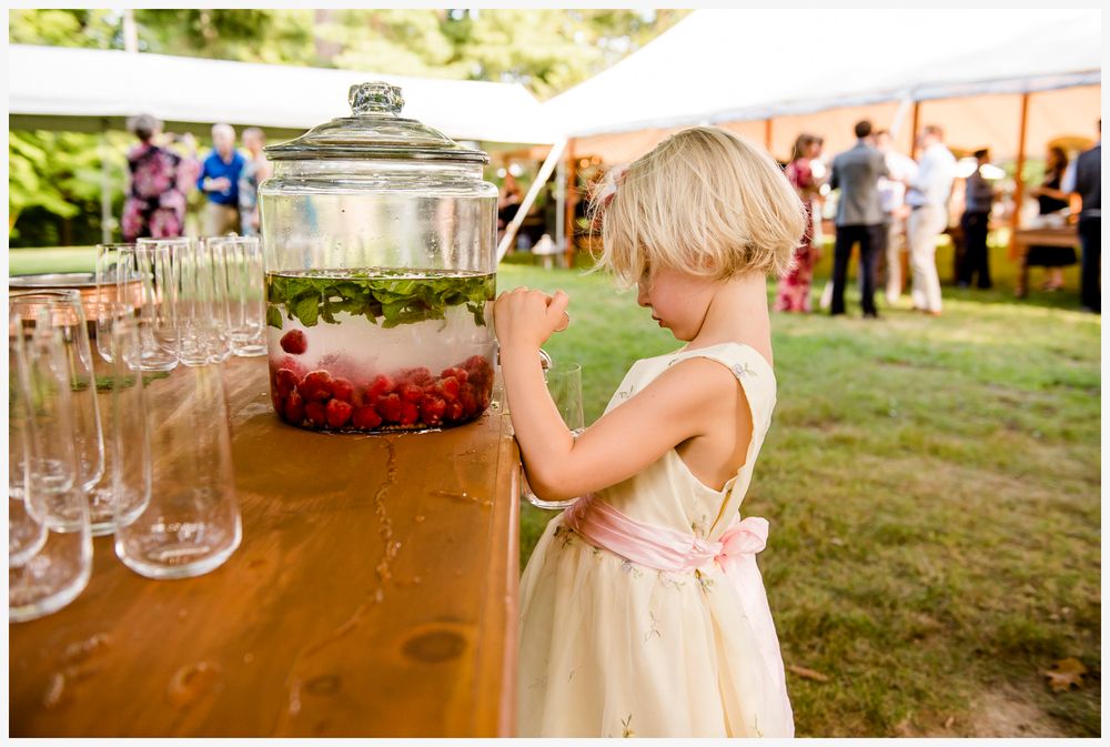 Young child reaching for drink dispenser at outdoor party refreshment table.