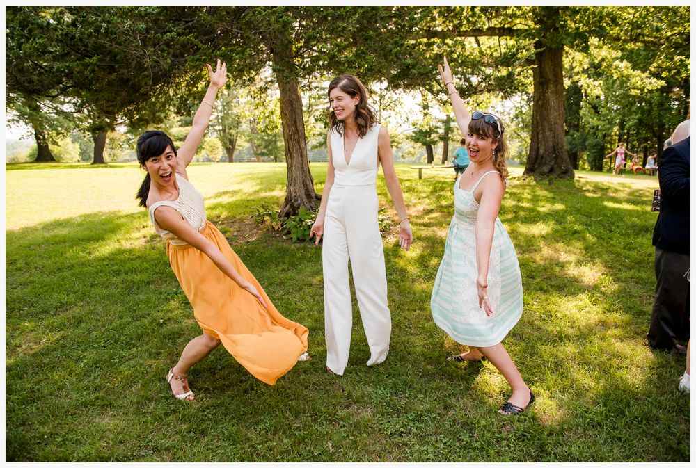 Three people dancing joyfully on grass during outdoor celebration.