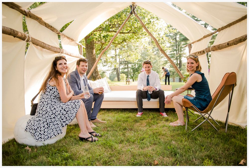 Group relaxing inside white canvas tent during outdoor event.