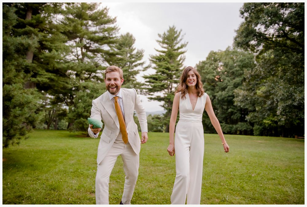 A couple dressed in coordinating white outfits dance joyfully on a scenic grassy lawn.