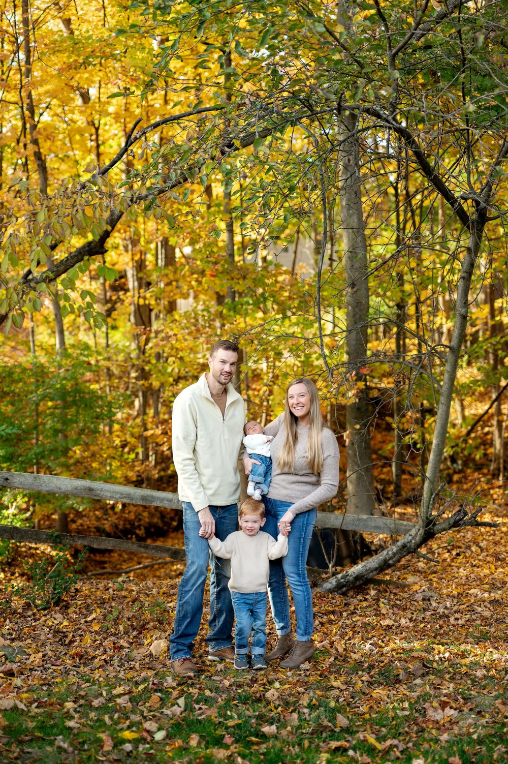 Smiling family of four posing among vibrant yellow fall foliage in a wooded park.