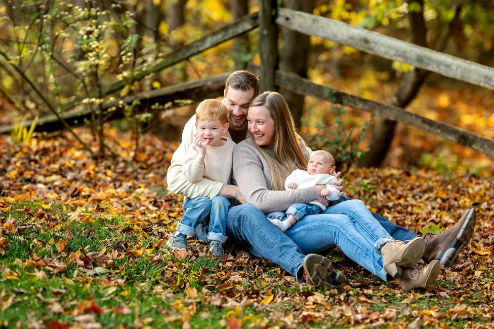 Loving family of four cuddling among golden fall leaves in a wooded setting.